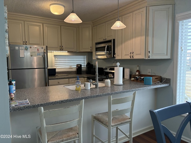 kitchen featuring appliances with stainless steel finishes, a textured ceiling, hanging light fixtures, and a breakfast bar area