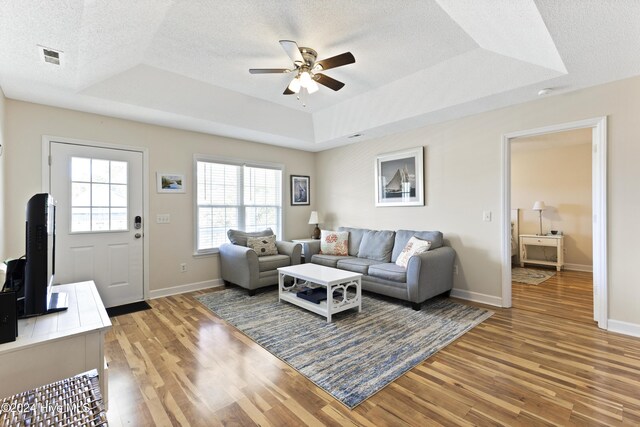 living room with hardwood / wood-style floors, a textured ceiling, and a tray ceiling