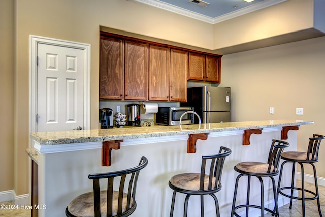 kitchen featuring tile patterned floors, stainless steel appliances, ornamental molding, light stone counters, and a breakfast bar area