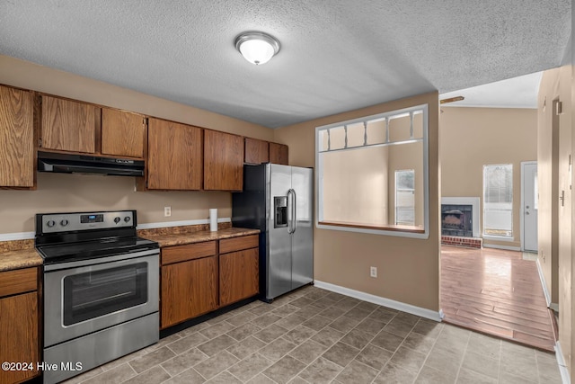 kitchen featuring stainless steel appliances, light hardwood / wood-style floors, a textured ceiling, vaulted ceiling, and a fireplace