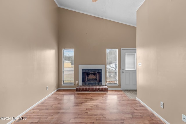 unfurnished living room with a brick fireplace, high vaulted ceiling, light hardwood / wood-style flooring, and crown molding