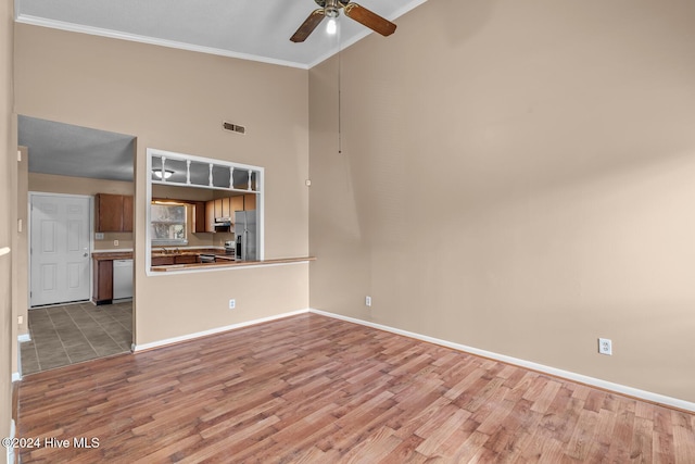 unfurnished living room with ceiling fan, light hardwood / wood-style floors, a towering ceiling, and ornamental molding