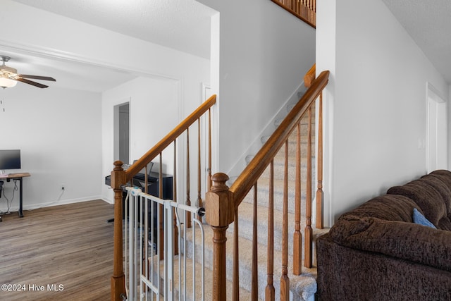 stairs featuring ceiling fan, wood-type flooring, and a textured ceiling