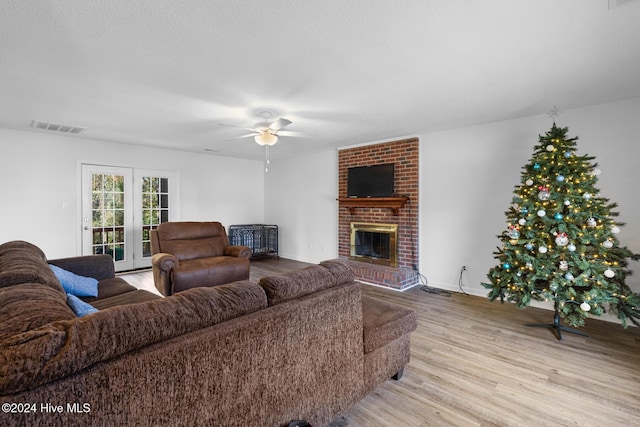 living room featuring ceiling fan, a fireplace, light hardwood / wood-style floors, and a textured ceiling