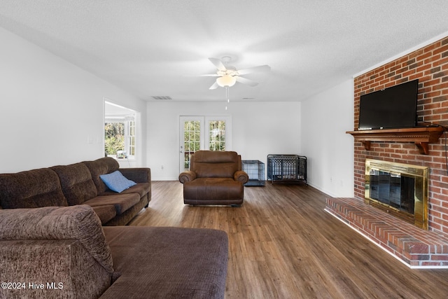 living room featuring hardwood / wood-style floors, ceiling fan, a fireplace, and a textured ceiling