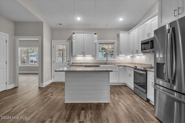 kitchen with white cabinets, appliances with stainless steel finishes, a kitchen island, and light stone countertops