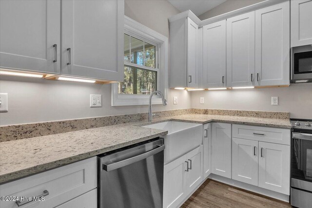 kitchen featuring hardwood / wood-style floors, white cabinets, sink, light stone countertops, and stainless steel appliances