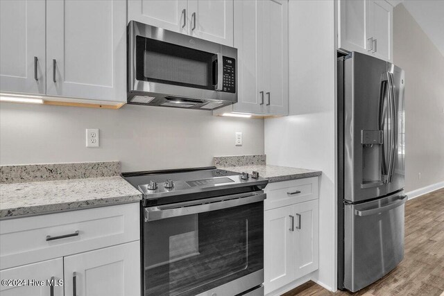 kitchen featuring white cabinets, light stone counters, light wood-type flooring, and appliances with stainless steel finishes