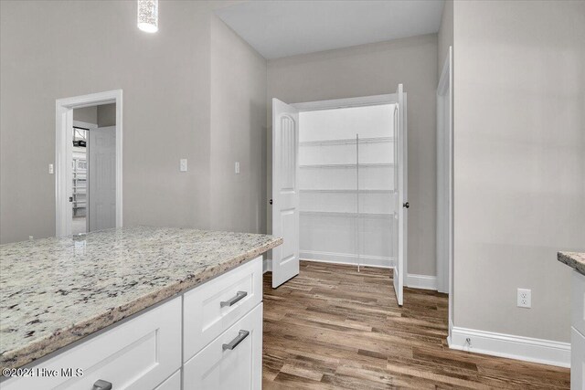 kitchen with light stone countertops, white cabinets, and wood-type flooring