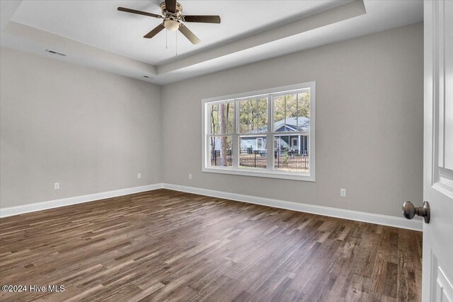 spare room with a tray ceiling, ceiling fan, and dark hardwood / wood-style flooring