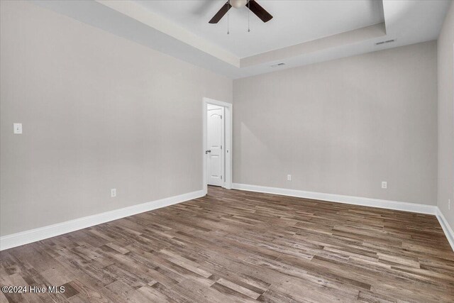 spare room with wood-type flooring, a tray ceiling, and ceiling fan