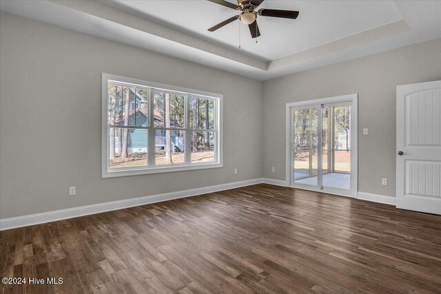 empty room featuring a tray ceiling, ceiling fan, and dark wood-type flooring