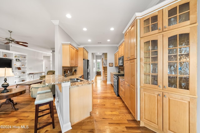 kitchen with kitchen peninsula, a kitchen breakfast bar, appliances with stainless steel finishes, light stone counters, and light hardwood / wood-style flooring