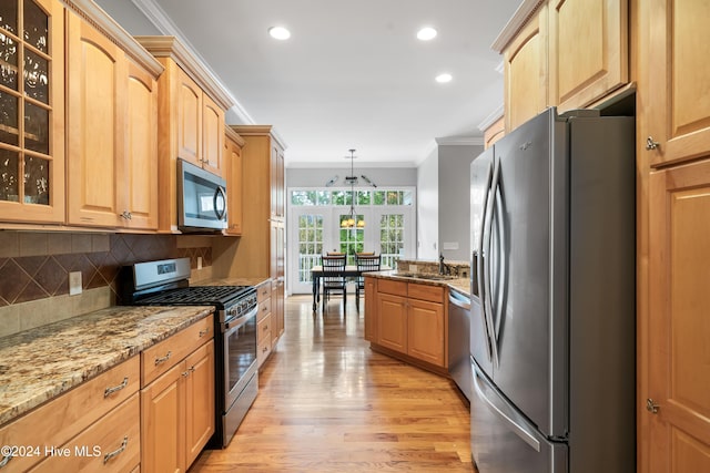 kitchen featuring hanging light fixtures, light stone counters, crown molding, appliances with stainless steel finishes, and light wood-type flooring