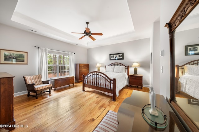 bedroom featuring ceiling fan, a raised ceiling, and light wood-type flooring