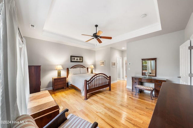 bedroom with ceiling fan, light hardwood / wood-style floors, and a tray ceiling