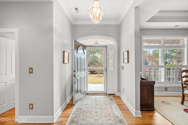 foyer entrance with ornamental molding, a notable chandelier, and light wood-type flooring