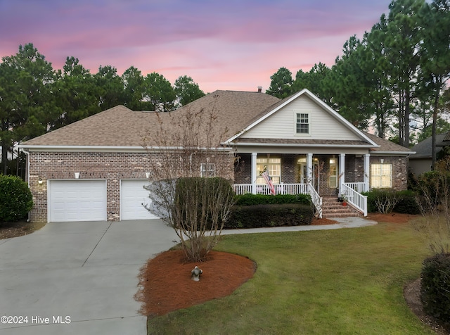 view of front of property featuring covered porch, a yard, and a garage