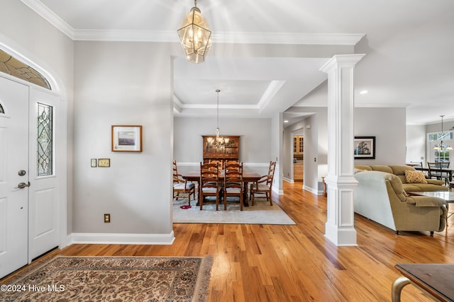 foyer entrance featuring decorative columns, ornamental molding, light wood-type flooring, and an inviting chandelier