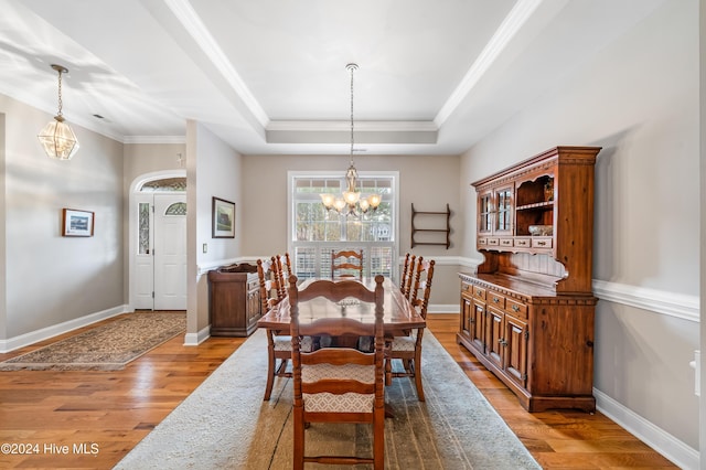 dining room featuring a tray ceiling, crown molding, light hardwood / wood-style flooring, and a notable chandelier