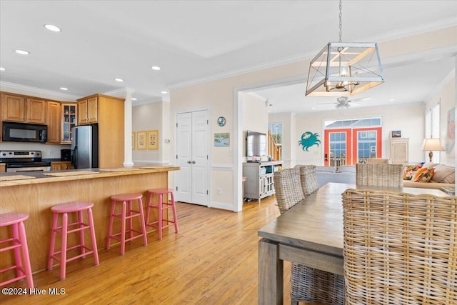 kitchen with a kitchen bar, appliances with stainless steel finishes, french doors, ornamental molding, and light hardwood / wood-style floors