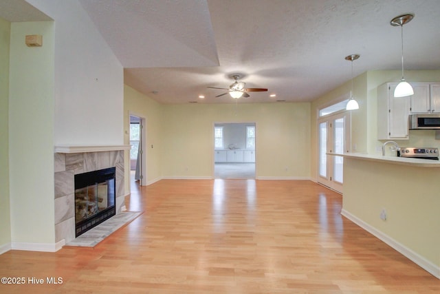 unfurnished living room with a tile fireplace, light hardwood / wood-style flooring, ceiling fan, and a healthy amount of sunlight