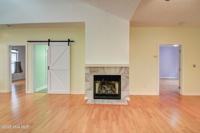 unfurnished living room featuring lofted ceiling, hardwood / wood-style flooring, a barn door, a textured ceiling, and a tiled fireplace