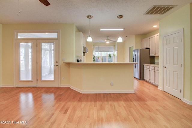 kitchen with white cabinets, kitchen peninsula, light hardwood / wood-style flooring, and hanging light fixtures