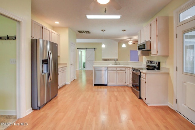 kitchen featuring appliances with stainless steel finishes, a barn door, light hardwood / wood-style floors, white cabinetry, and hanging light fixtures