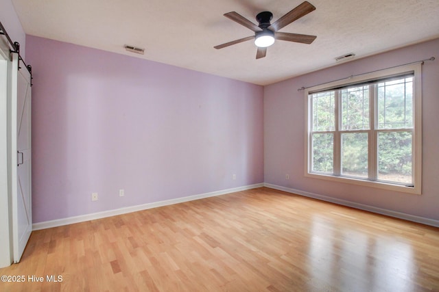 spare room featuring a barn door, ceiling fan, and light hardwood / wood-style flooring