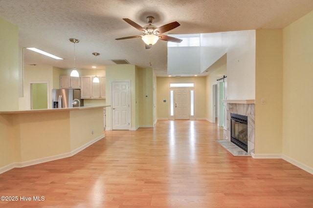 unfurnished living room featuring ceiling fan, a barn door, a textured ceiling, and light hardwood / wood-style flooring