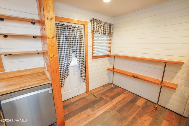 kitchen featuring dark wood-type flooring, stainless steel dishwasher, and wooden walls