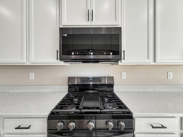 room details with black gas stove, white cabinetry, and light stone counters