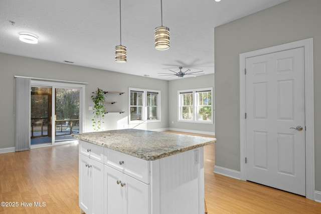 kitchen with a textured ceiling, decorative light fixtures, light hardwood / wood-style floors, a kitchen island, and white cabinetry