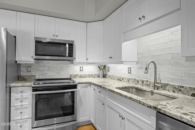 kitchen with light stone countertops, stainless steel appliances, tasteful backsplash, white cabinets, and sink