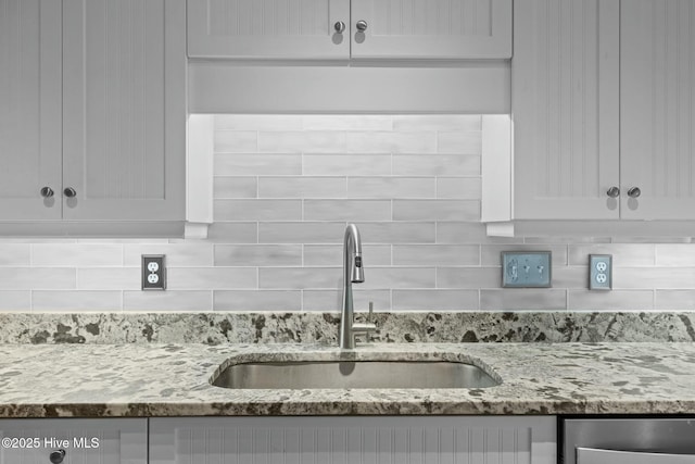 room details featuring sink, white cabinets, decorative backsplash, and light stone countertops