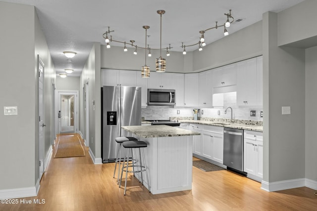 kitchen with a center island, decorative light fixtures, stainless steel appliances, decorative backsplash, and white cabinetry