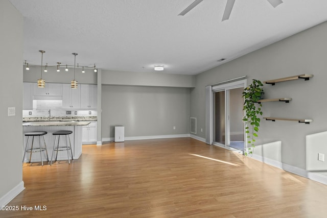 unfurnished living room with sink, a textured ceiling, light wood-type flooring, and ceiling fan