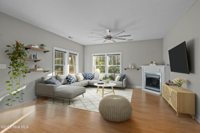 living room with a textured ceiling, ceiling fan, and light hardwood / wood-style flooring