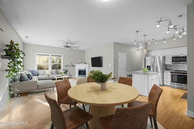 dining room with a textured ceiling, ceiling fan, and light hardwood / wood-style flooring