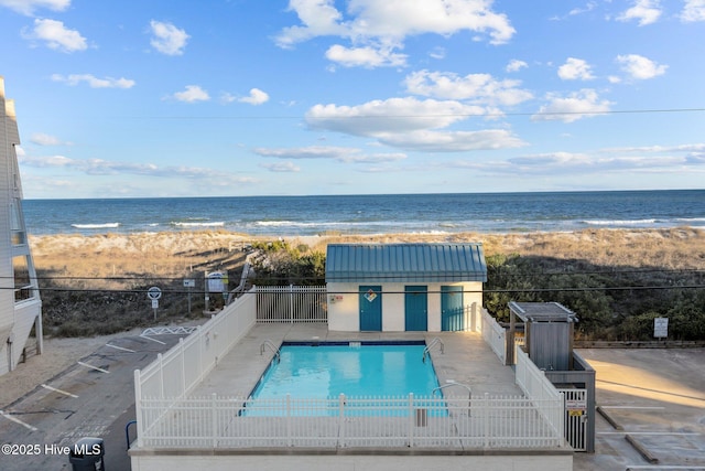 view of swimming pool featuring a water view, a beach view, and a patio