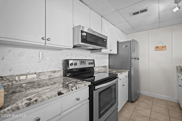 kitchen with light stone countertops, appliances with stainless steel finishes, a drop ceiling, light tile patterned floors, and white cabinets