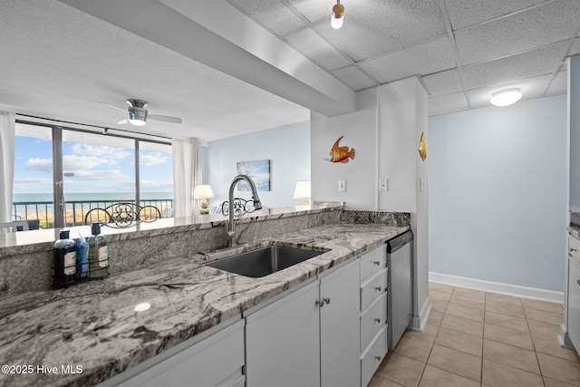 kitchen featuring white cabinetry, dishwasher, sink, light stone countertops, and a water view