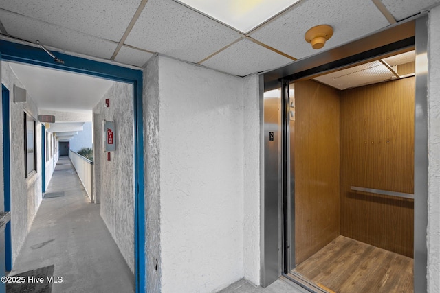 hall with concrete flooring, a paneled ceiling, and elevator