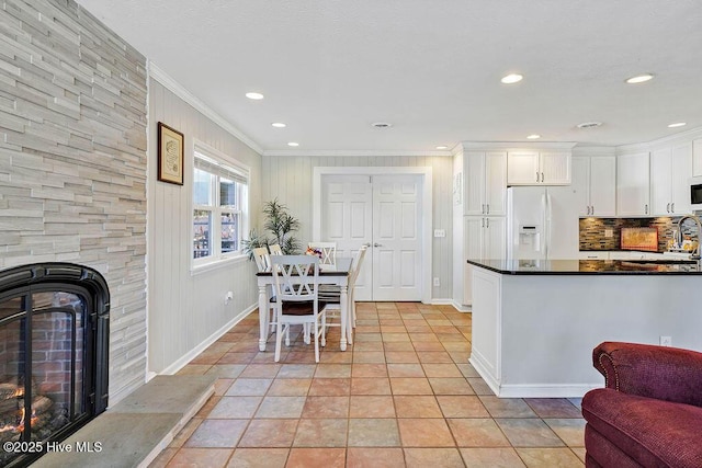 kitchen featuring a large fireplace, crown molding, white appliances, white cabinetry, and light tile patterned floors