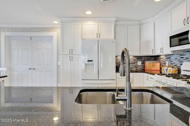 kitchen with white cabinetry, white appliances, dark stone countertops, ornamental molding, and sink