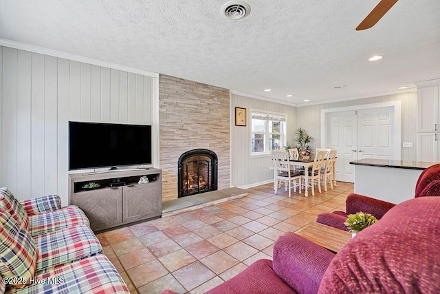 tiled living room featuring a textured ceiling, ornamental molding, wood walls, and a stone fireplace