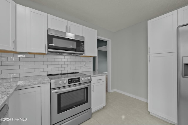 kitchen featuring backsplash, light stone counters, stainless steel appliances, light tile patterned floors, and white cabinetry