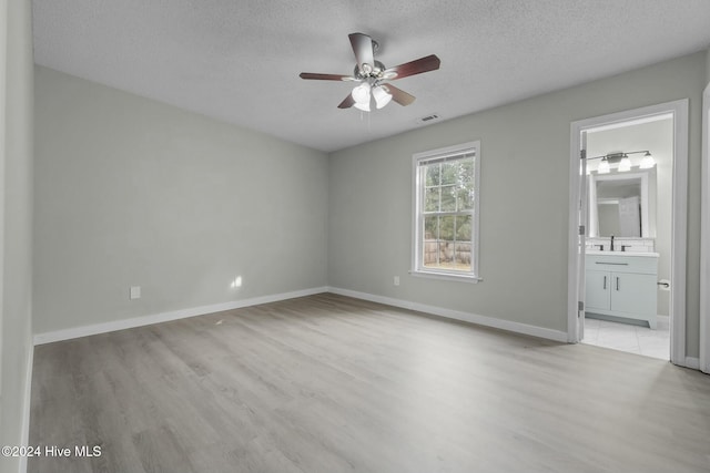 unfurnished bedroom with a textured ceiling, connected bathroom, light hardwood / wood-style flooring, and ceiling fan