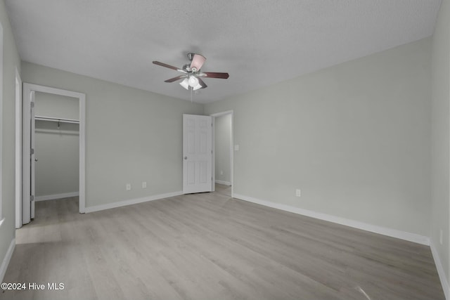 unfurnished bedroom with a walk in closet, light hardwood / wood-style flooring, ceiling fan, a textured ceiling, and a closet